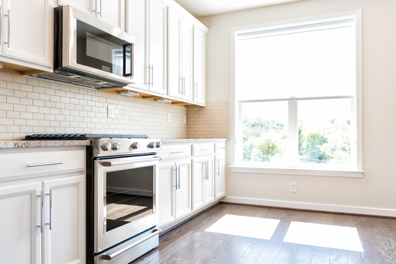 Modern gray, brown neutral kitchen features front cabinets with granite countertops and tile backsplash, window in contemporary home, house, apartment