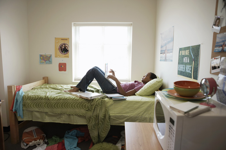 Young woman lying on bed using laptop computer, in student dormitory