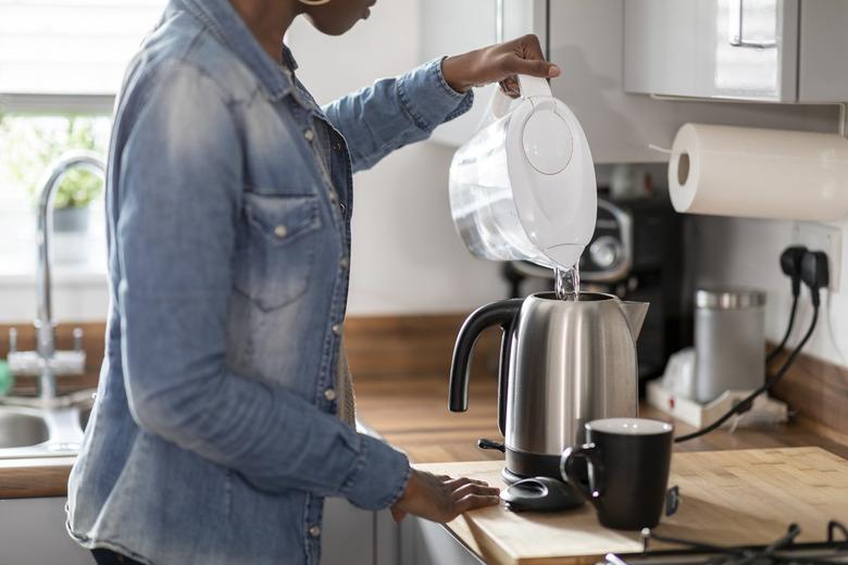 Woman pouring water into kettle in kitchen