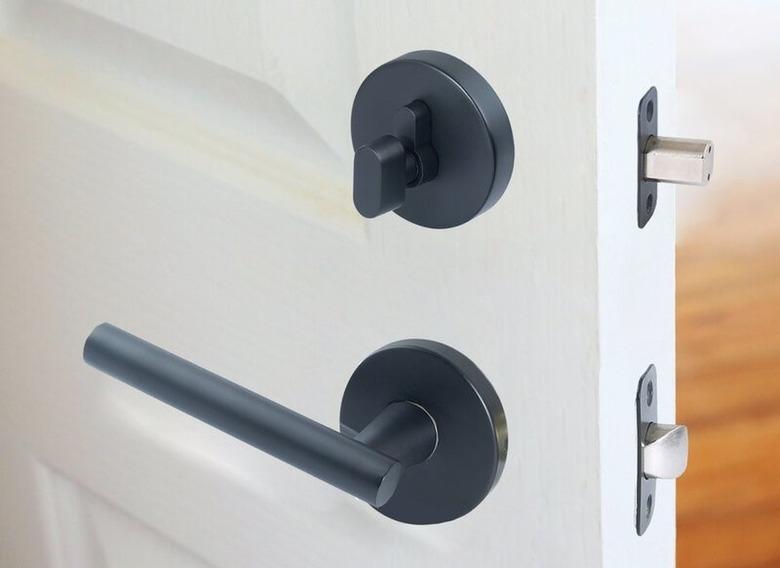 Black metal door handle and matching single cylinder deadbolt lock on a partially open white door