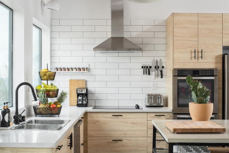 corner of kitchen with light wood cabinetry, stove hood, white subway tile walls