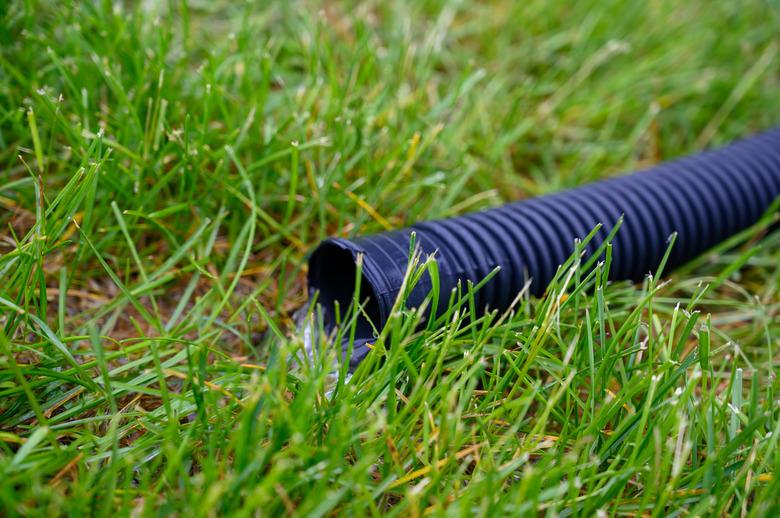 Residential sump pump discharging water from the end of a flexible black hose.