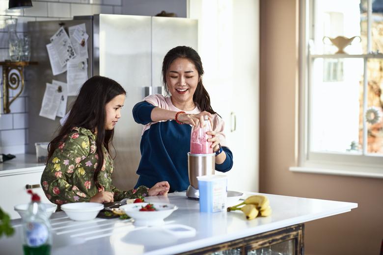 Woman using smoothie maker with daughter watching in kitchen