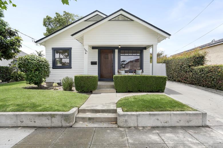 white craftsman home with green grass and some evergreen shrubs