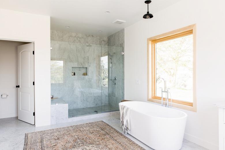 bathroom with freestanding white tub, walk-in shower with glass door, large window, multicolored area rug