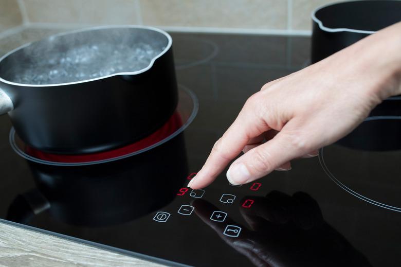 Close Up Of Woman Adjusting Temperature Of Halogen Hob In Kitchen