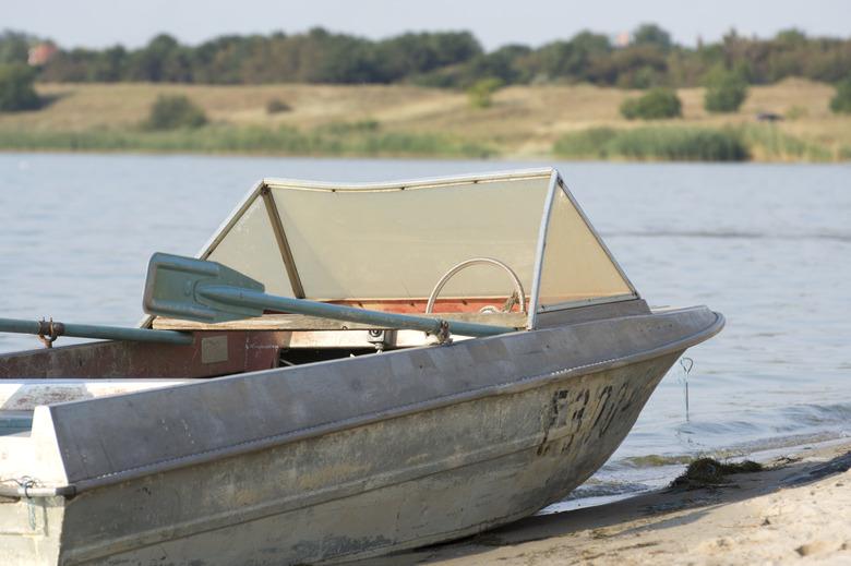 Old aluminum fishing boat by lake or river.