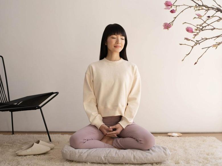 Marie Kondo meditating on a pillow in front of a white wall.