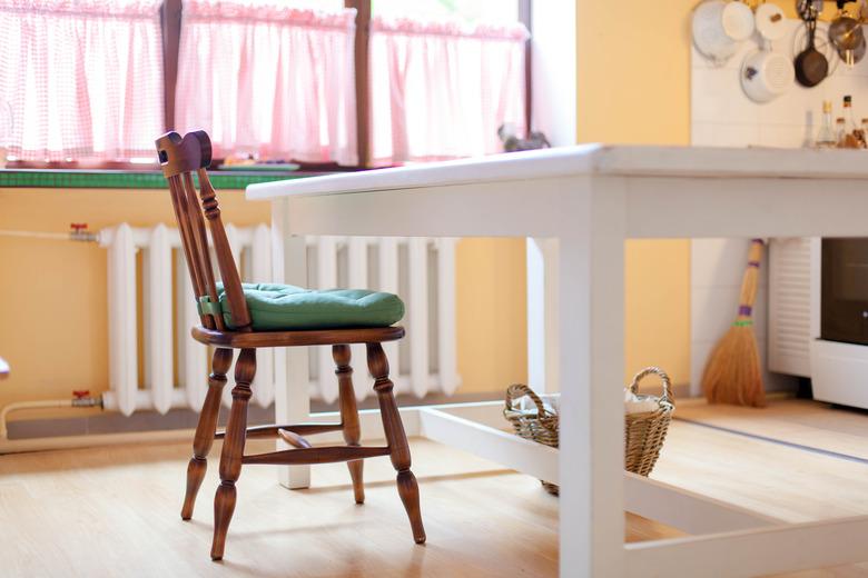 Kitchen scene with white table, wooden chair and green cushion. Cozy home with wisker basket on floor and heating battery under big window.