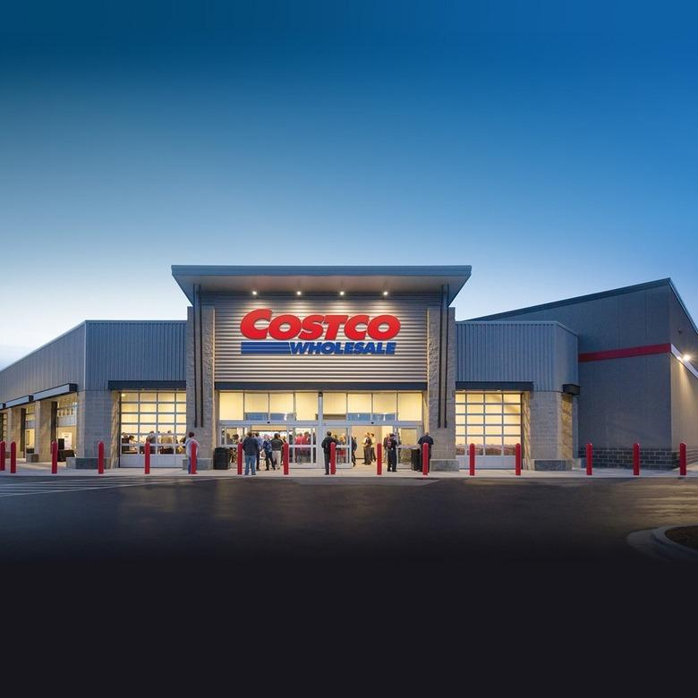 The exterior of a Costco warehouse at twilight. There is a red and blue sign at the front that says "Costco Wholesale" with people outside entering the store.