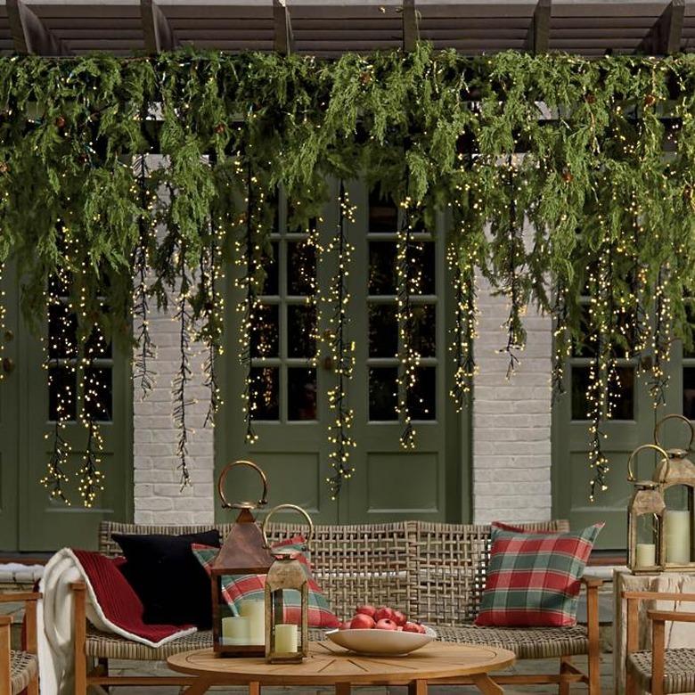 exterior Christmas decorations with Draped evergreen garland with meteor lights, wicker couch, pillows and wood outdoor coffee table, french doors.