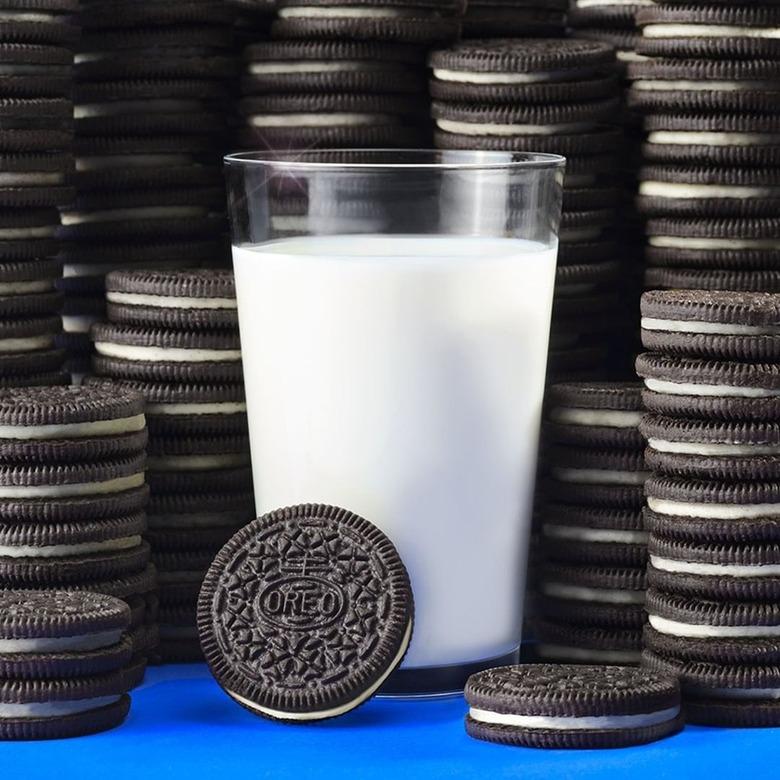 Stacks of Oreo cookies surrounding a full glass of milk on a blue table