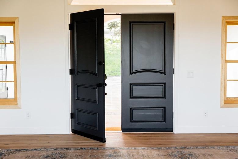 Double doors made of dark wood, the main entrance to the home. Two windows with light wood frames, one on either side of the door.