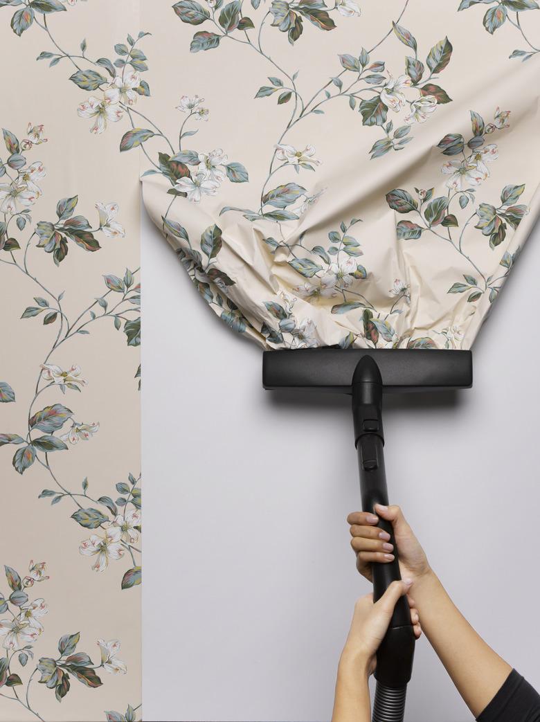 Woman vacuuming wallpaper from wall, close-up