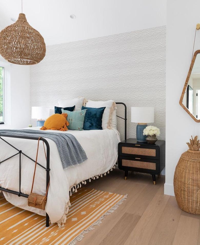 Bedroom with black iron bed frame, white bedding, woven light fixture, and bright pillows in yellow and shades of blue