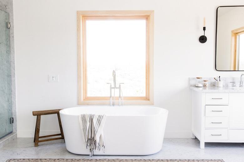 white bathtub in front of window and next to white vanity sink