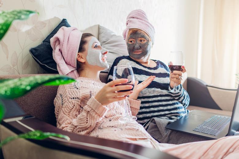 Mother's day. Mother and her adult daughter applied facial masks at home. Women talking while having wine