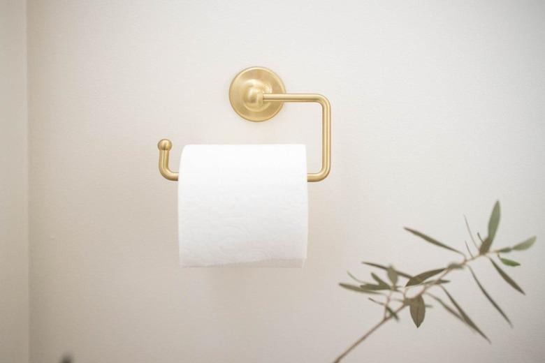 Gold toilet paper holder with toilet paper and a leaf branch