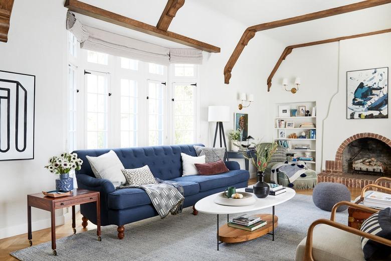 navy blue living room idea by Emily Henderson with tufted blue sofa and brick fireplace