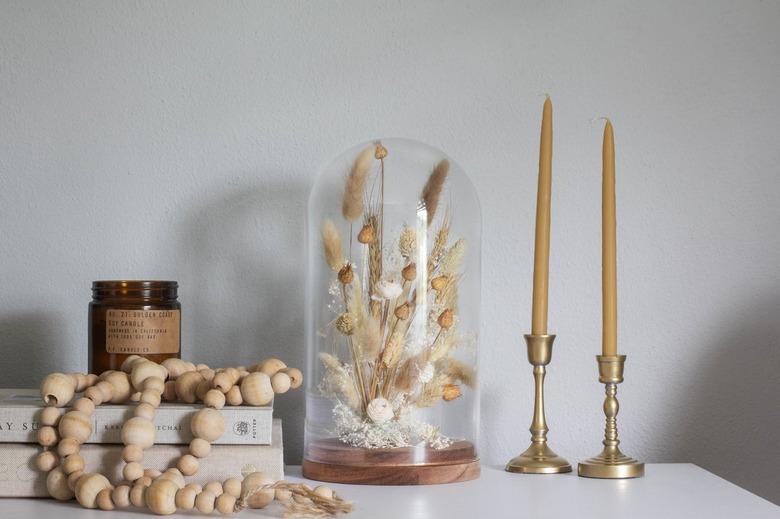 Cloche with dried plants next to candlesticks and wood bead necklace