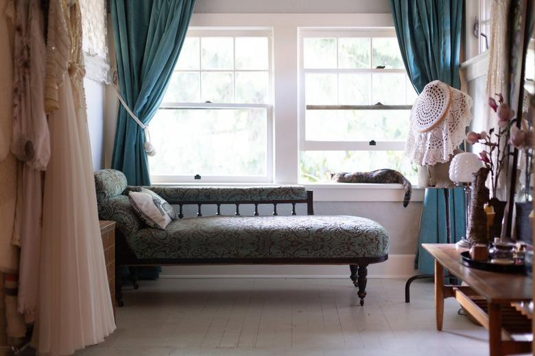 A floral upholstered daybed, blue curtains, and a cat laying on a windowsill. Vintage accent pieces.