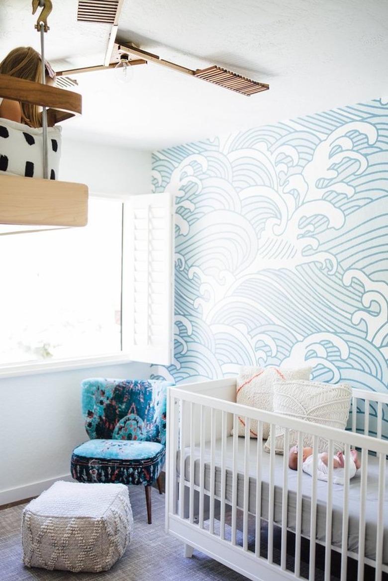 Modern nursery with wave pattern wallpaper, blue chair, white crib.