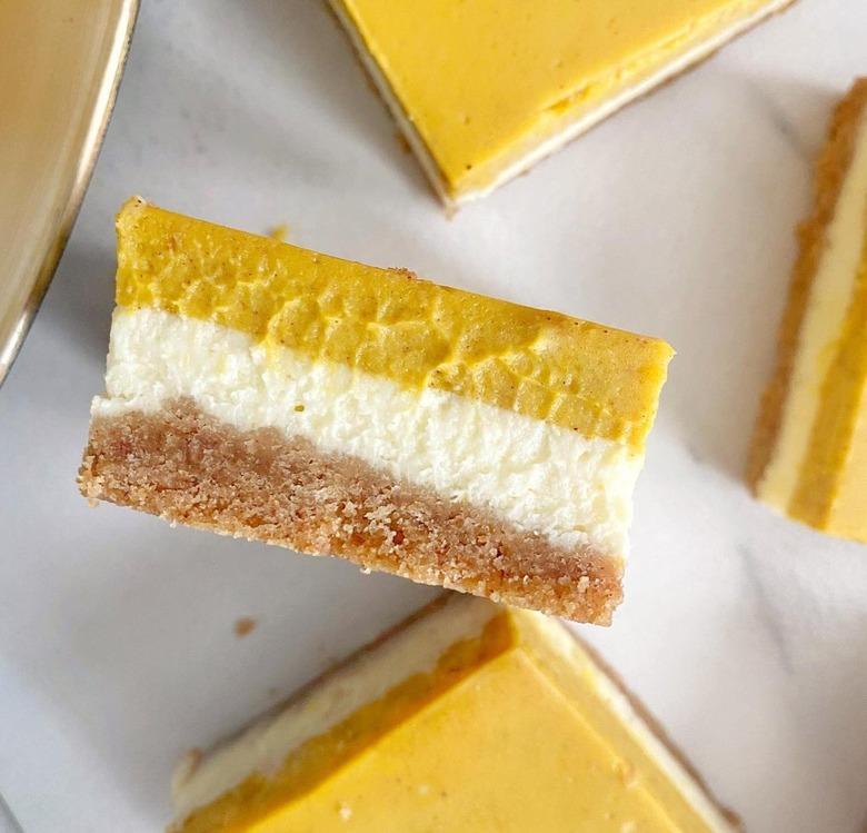 A dessert bar featuring a stripe of orange pumpkin filled, a cheesecake stripe, and a light brown stripe of crust.