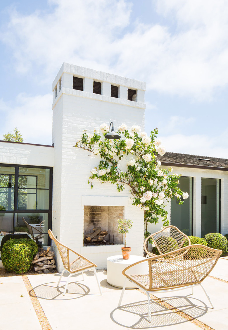 painting exterior brick on white painted brick house with outdoor fireplace, patio, lounge chairs and couch, rose vine.