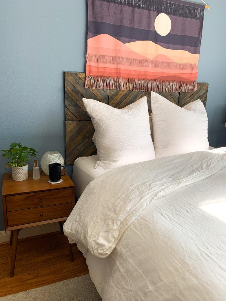 Bedroom with blue walls, wooden headboard, nightstand, and white bedding.