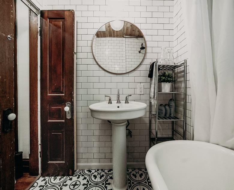 Pedestal Sink Storage Ideas in Bathroom with white pedestal sink, white subway tile, clawfoot tub, round mirror, metal shelves.