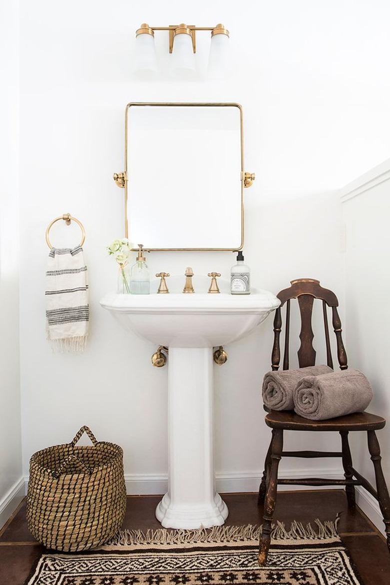 Pedestal Sink Storage Ideas in Bathroom with white pedestal sink, rectangle mirror, vintage wood chair, towels, basket.