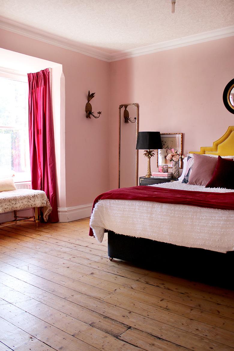 pink bedroom with dark pink drapery and bedding and wood flooring