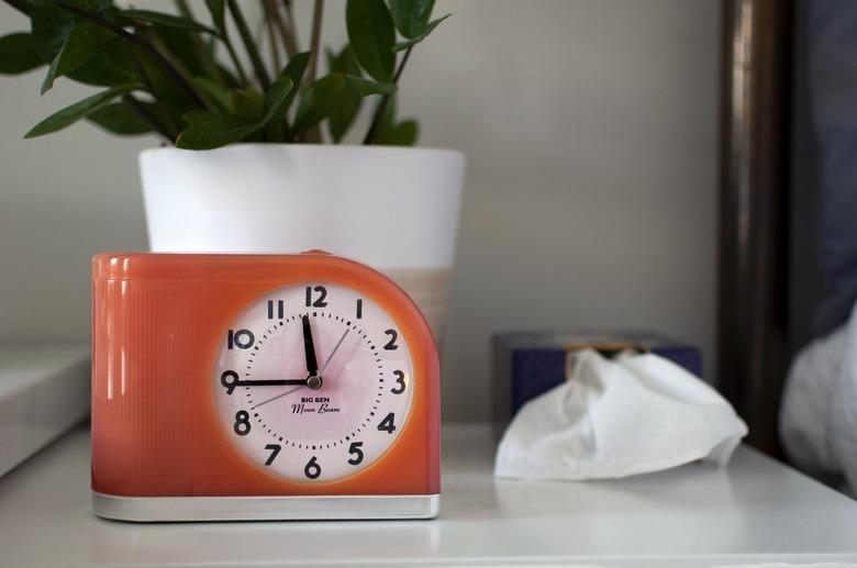 An orange retro style clock on a white desk with a plant