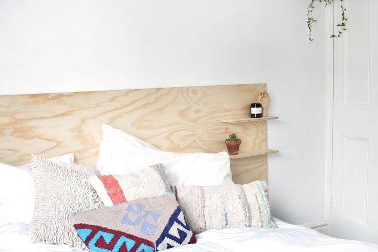 a headboard made out of a sheet of unfinished plywood with two shelves mounted on it