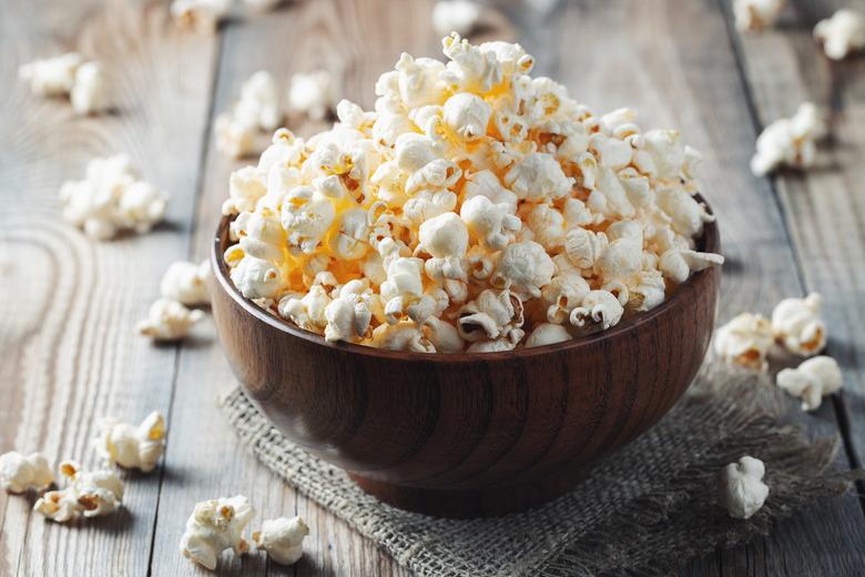 A wooden bowl of salted popcorn at the old wooden table. Dark background. selective focus