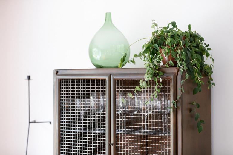 Houseplant on dining room cabinet with green glass vase