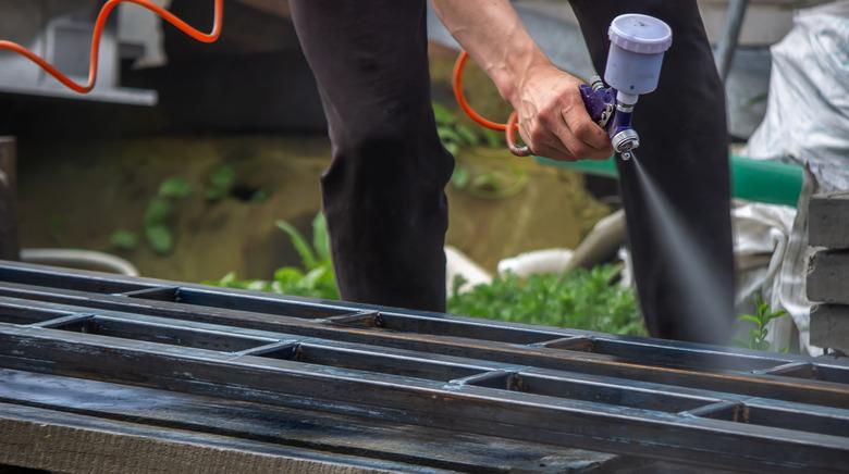 A man with a paint sprayer paints a metal structure on the street.