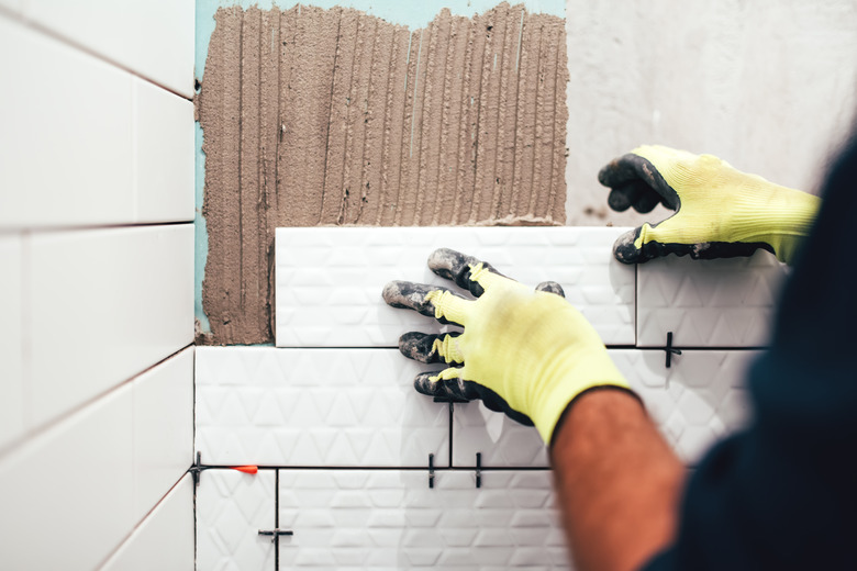 construction worker installing small ceramic tiles on bathroom walls and applying mortar with trowel