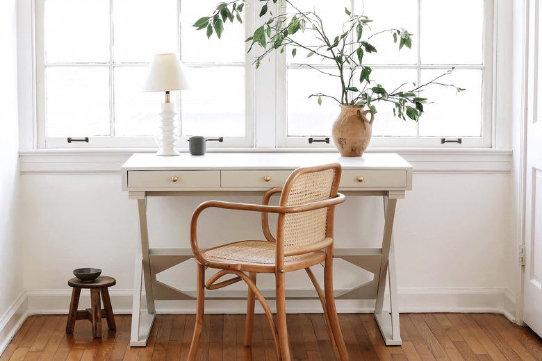 Home office desk painted with light gray milk paint in front of window with lamp and vase