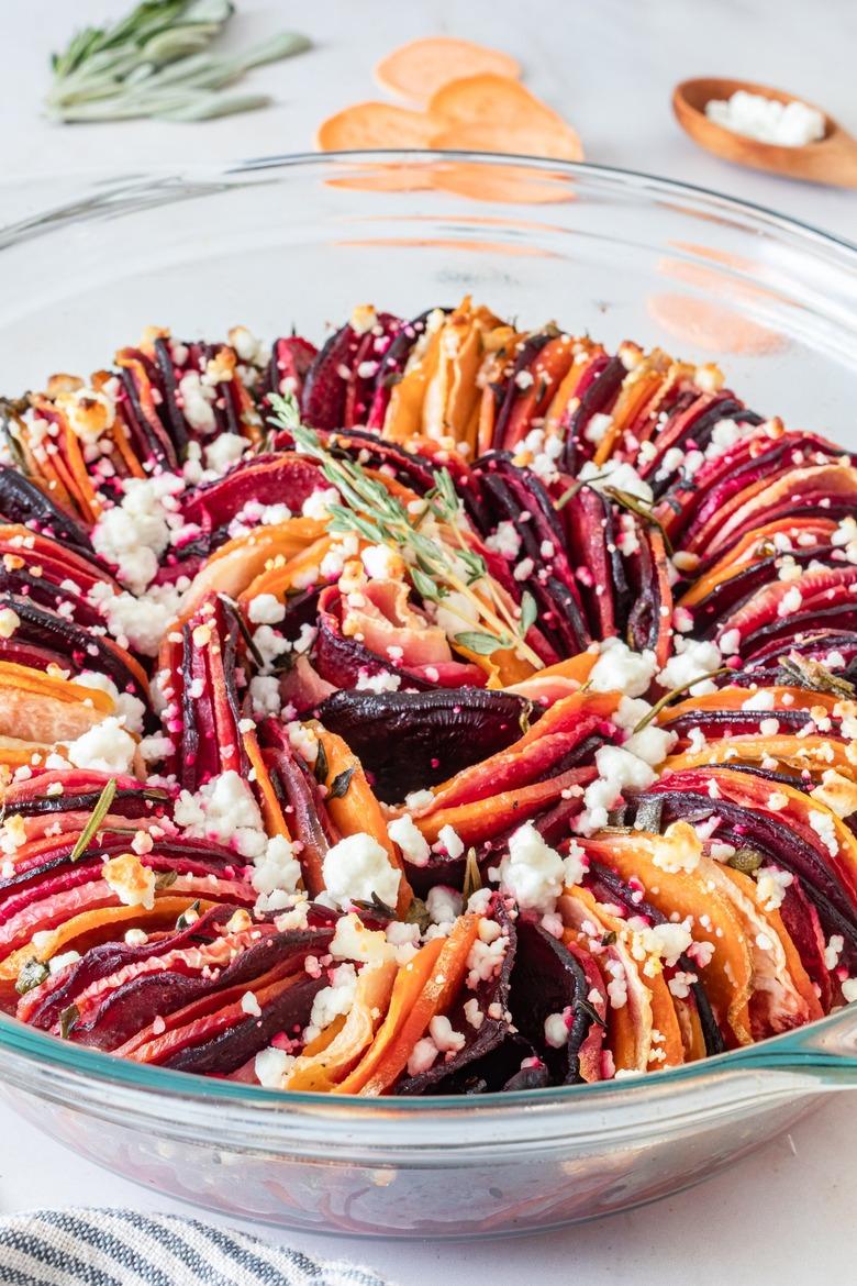 A root vegetable and goat cheese bake in a glass pie pan featuring red, orange, and dark pink root vegetables sprinkled with goat cheese.