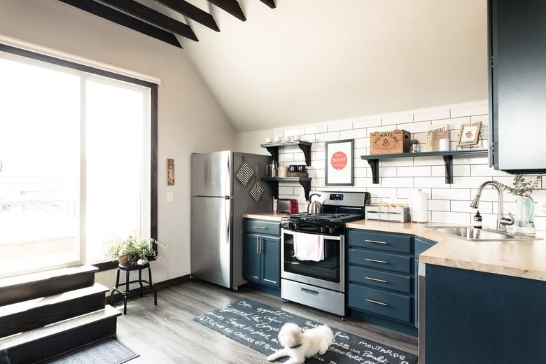 Kitchen with white tiles and blue cabinets with large windows and a dog on floor