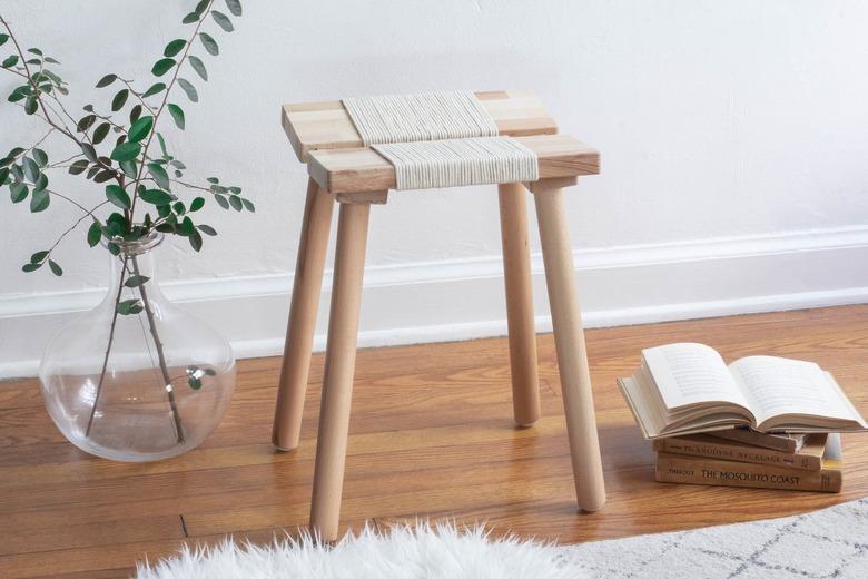 IKEA wood stool with rope on wood floor with plant in clear vase and stack of books