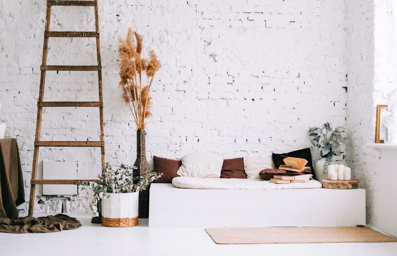 Interior design of bright living room with white walls and couch bench with pillows. Dried high plants and wooden ladder near wall.