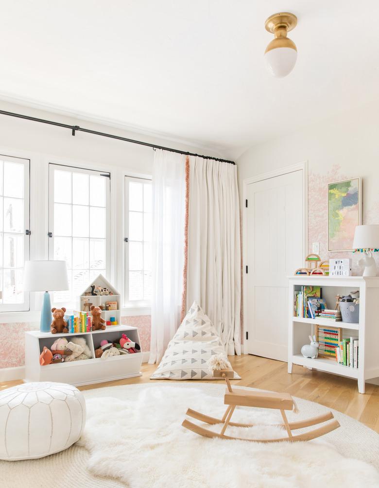 Scandinavian nursery idea with wood rocking horse on top of layered rugs in front of large windows