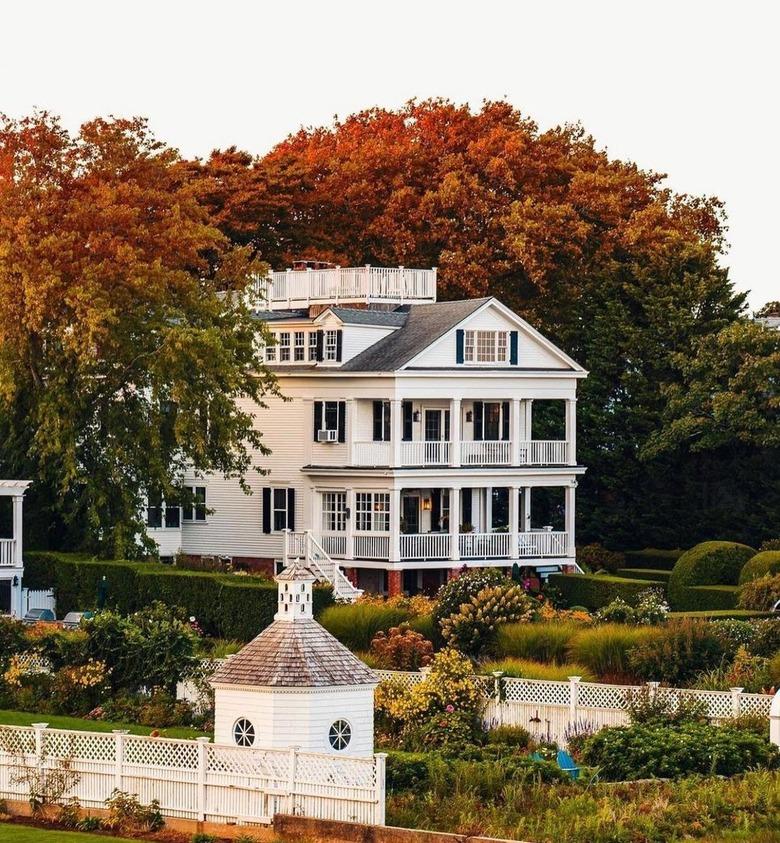 A white house with a balcony overlooking greenery with autumnal-colored trees surrounding it in Edgartown, MA.