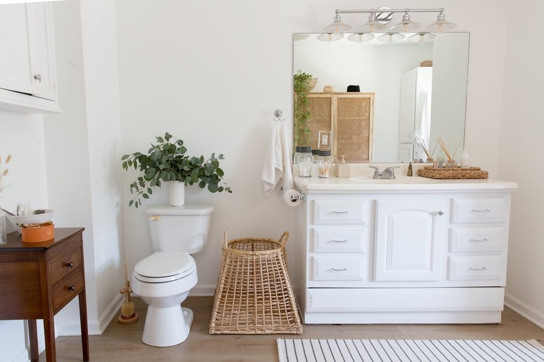 Shabby Chic Bathroom Storage in Bathroom with white vanity, mirror, basket, end table, toilet, rug, plant.