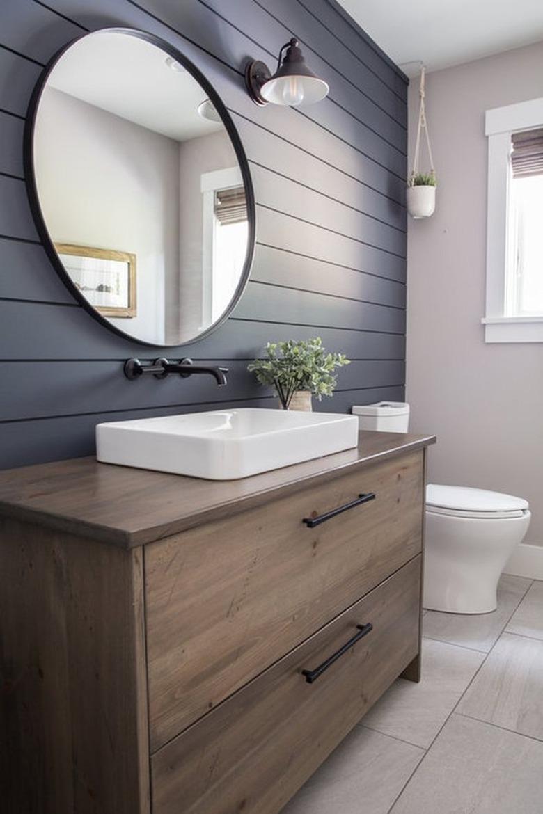 Gray shiplap wall in farmhouse style bathroom, wood vanity, round mirror.