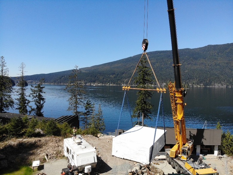 A crane lowering a shipping container pool into a yard.