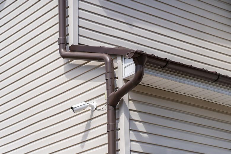 circuit TV CCTV security camera mounted on corner of building with siding facade next to brown gutter pipe