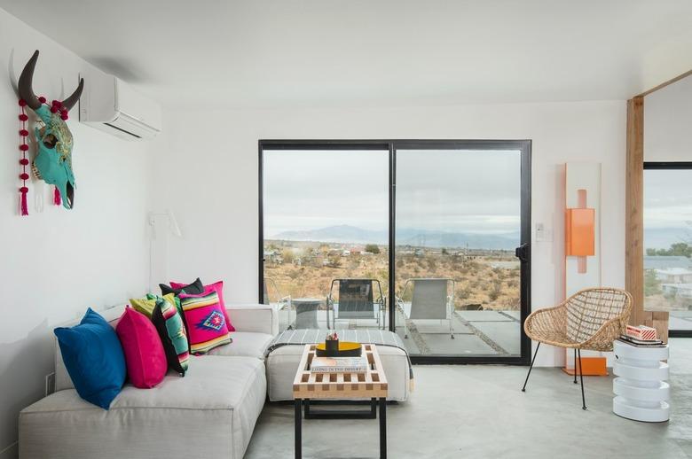 Minimalist living room with a gray sofa with colorful pillows, large windows and wood accents